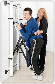 A young man demonstrating the use of the Rifton Support Station with the aid of a caregiver.