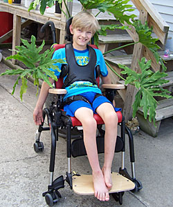 A young boy smiles from his Rifton Activity chair as he sits on the patio in the fresh air 