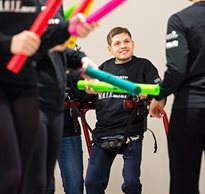A young man with disabilities in a gait trainer smiles as he performs his dance movements