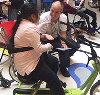 A Rifton member gives a high five to a Laremont student in a special needs trike while other students move around in their adaptive equipment behind them 