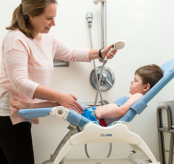 A caregiver holds a shower want as she prepares to bath a young boy with special needs in the Rifton Wave adaptive bathing system.