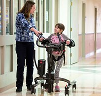 A therapist helps a young girl in a TRAM with gait control as she walks down the hallway of a school 