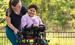 A caregiver assists a young girl walking in a Rifton Activity Chair.