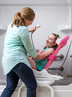 A caretaker bathes a young girl in a Rifton Wave bath chair.