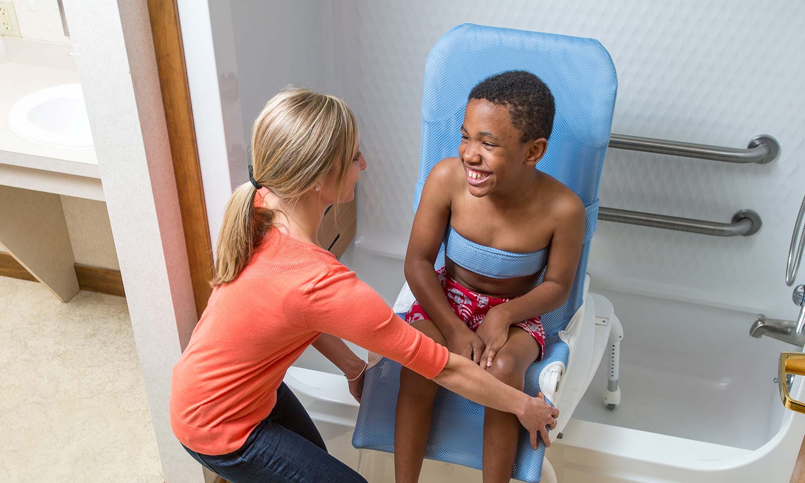 A boy sits in a Rifton Wave Bath Chair and talks with his caregiver.