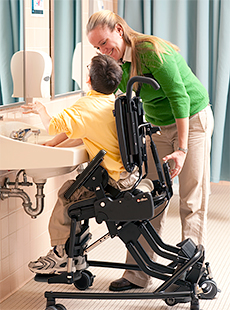 A therapist activates the Rifton Activity Chair's tilt-in-space feature to allow a school-aged boy to wash his hands at a sink