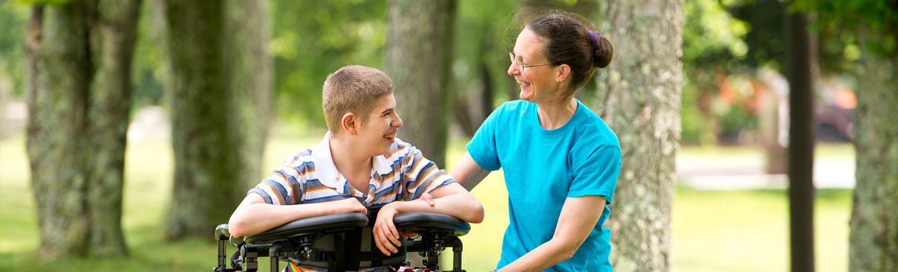 A boy walks in a Rifton Pacer and talks with his caretaker.