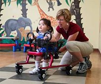 A therapist helps position a young girl to be a walker in a mini Rifton Pacer Gait Trainer