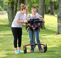 A young man walking outside in a Rifton Pacer gait trainer, assisted by a caregiver.