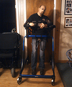 Casey Breyette stands in his blue Pacer XL adult gait trainer helping him ambulate around his home for a quicker recovery from his traumatic brain injury