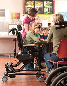 A young girl in a cafeteria eating lunch in a Rifton active sitting chair