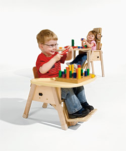 A young boy and girl demonstrating proper positioning in the Rifton Chair, smile as they play with colorful toys