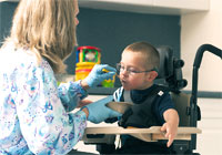 A young boy in his small Rifton Activity Chair gets spoon fed by a woman using the device as a feeding chair.