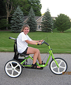 A teenager rides her green special needs bike on the pavement in front of her house