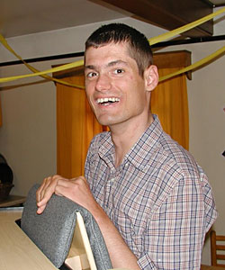 Duane stands and smiles at the camera with yellow streamers in the background for his birthday