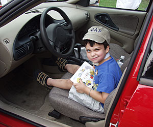 A young Scott Conlon gives a mischievous grin sitting inside a red car with a book on his lap