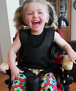 "A young girl in an adaptive chair laughs and smiles