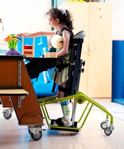 A young girl in a classroom setting can participate in classroom activities when in her standing device frame.
