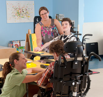 Two caregivers in a playroom with young adults with special needs work on head positioning and functional activities. 