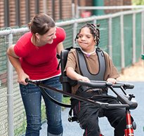 A caregiver smiles as she leans over helping a young girl with her special needs equipment