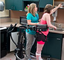 A therapist assists a CNS patient who is standing in a TRAM device practicing gait training during rehabilitation.