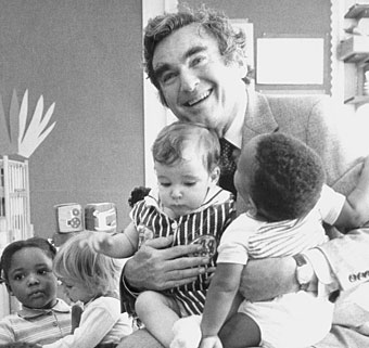 James Gallagher in a special education classroom full of children embraces two of them sitting on his lap. 