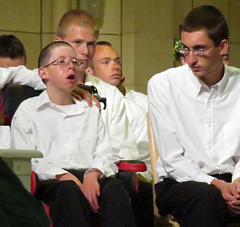 A young boy with special needs is surrounded by his friends and other graduates in the auditorium as he waits for his name to be called