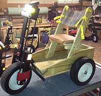 A personal energy transportation (pet) three wheeled, motorized bike made from wood and metal sitting on a table in a shop. 