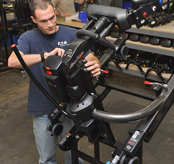 A worker in the Rifton warehouse adjusting settings on a Rifton TRAM special needs equipment surrounded by shelves filled with accessories