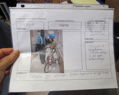 A therapist holds an example of a instruction sheet out of a positioning protocol book showing details on how to properly position one of the students
