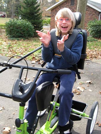 A girl smiles and claps her hands on a Rifton trike from Variety the Children's Charity