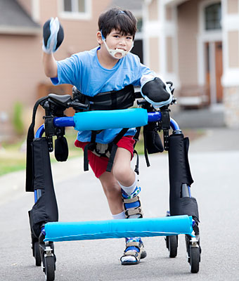 A young boy laughs as he walks down the driveway in a blue padded over-ground gait trainer