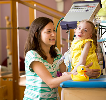 A young girl with a complex medical condition using Medicaid funded equipment while her therapist assists her