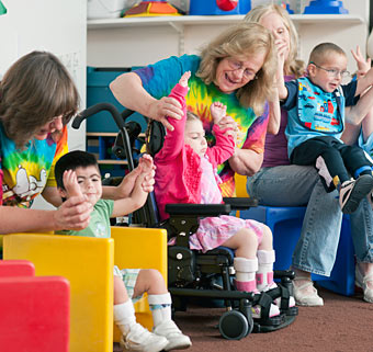 Educators and therapists sitting with children in a colorful special needs playroom, work as a team to help students practice their motor skills