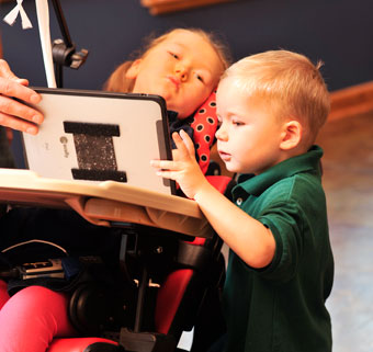 A young girl demonstrates active sitting to participate with her brother while they playing on a device