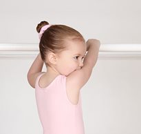 A little girl with cerebral palsy in a pink tutu holds onto a ballet bar as she learns to dance