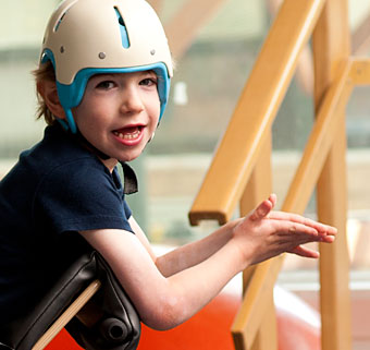 A young boy with spastic cerebral palsy smiles and claps his hand as while in a standing device