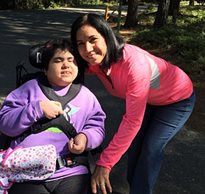 A mom leans over to take a picture with her daughter in a wheelchair on a trail at an inclusion camp 
