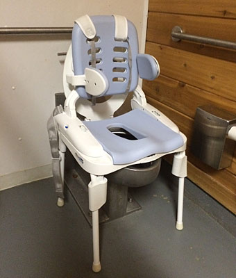 The Rifton HTS portable travel toilet shown over a toilet seat at a bathroom at a park facility