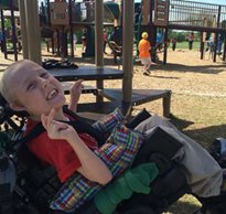 A young boy with special needs in a wheelchair on the playground at a park traveling for a field trip