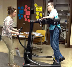 A TBI patient gets assistance from a therapist to find the proper positioning in the walking saddle on the TRAM.
