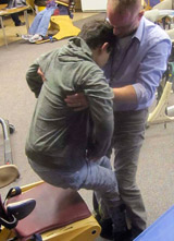 A therapist assists a TBI patient transferring him from a chair to a mat table.