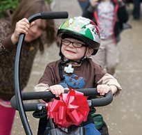 A young boy grins as he rides his adaptive tricycle from the Great Bike Giveaway