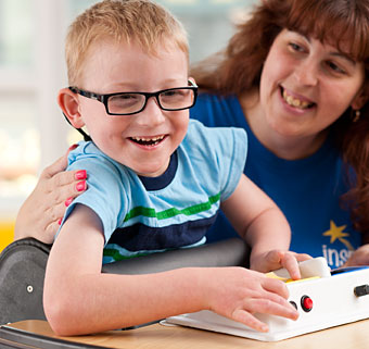 A therapist helps a young boy in a standing device as he plays with a toy