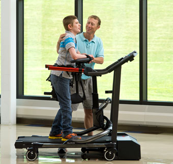 A boy works on dynamic gait training on treadmill with his therapist