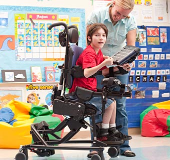 A therapist assists a child in adaptive chair using a computerized screen to practice motor learning tasks
