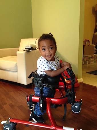 A young girl in a Rifton gait trainer smiles at the camera while practicing her motor skills to help with cognitive development