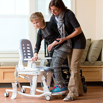 A teacher assists a student with a standing transfer to a commode.