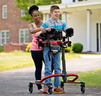 A caregiver assists a teenager using a medically necessary Rifton Pacer gait trainer outdoors