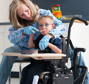 An occupational therapist helps feed a young boy in an activity chair during school lunch. 